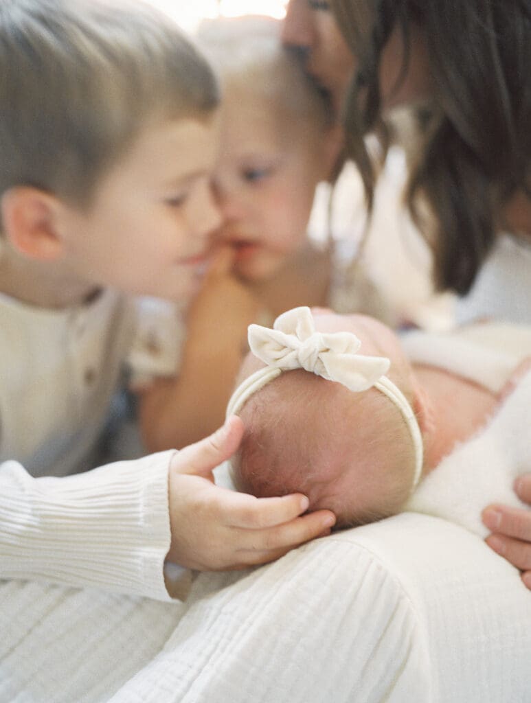 Big brother and sister kissing and hugging their newborn sister during an in home photo session.